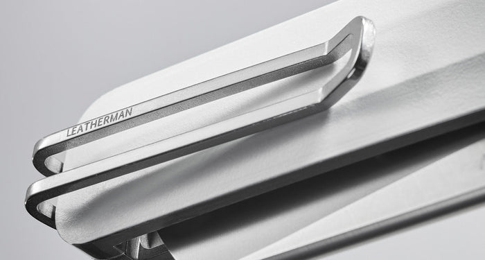 Close-up image of a Leatherman knife's sleek metal pocket clip, engraved with the Leatherman brand name, attached to a minimalist white handle against a soft gray background.