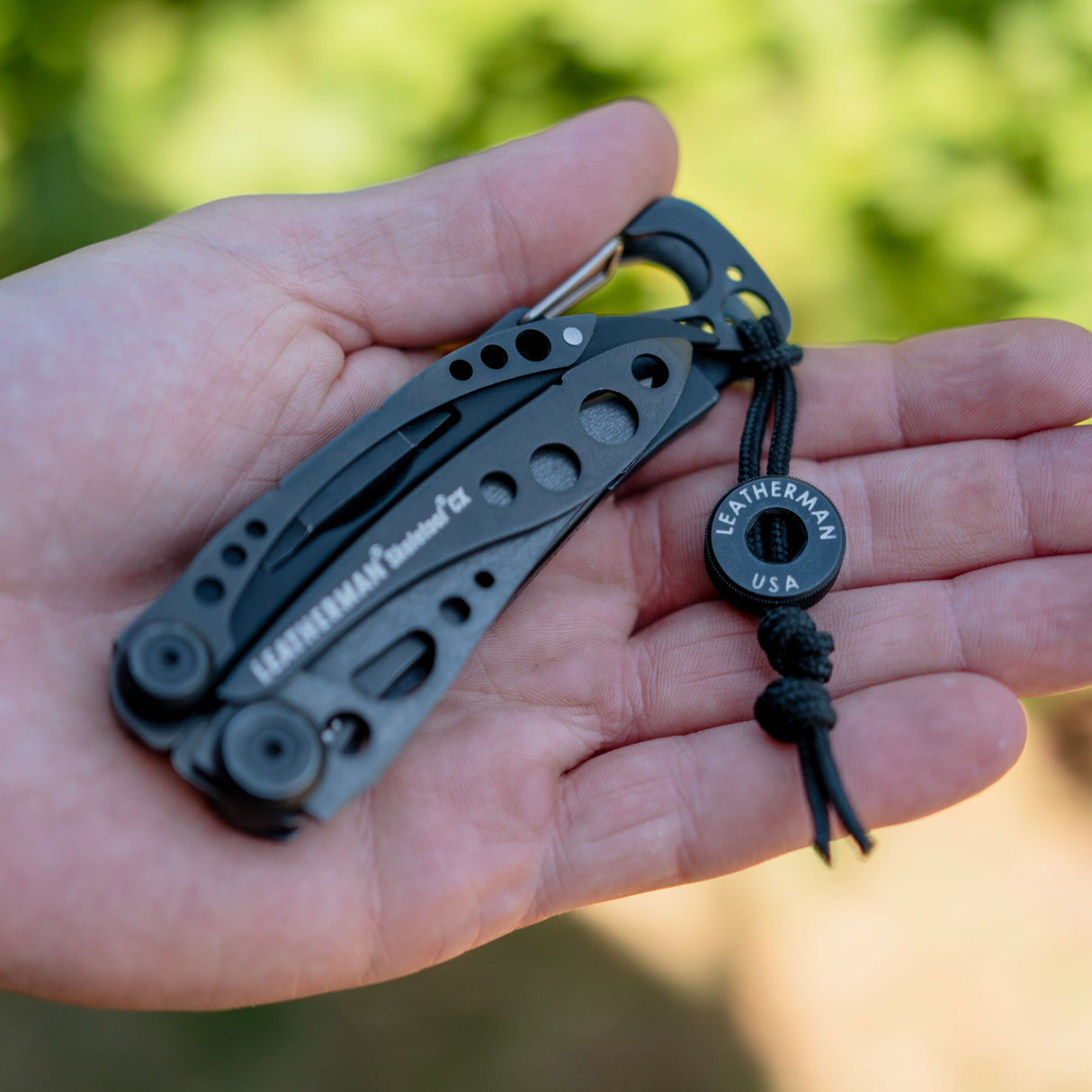 Translation missing: fr.Hand holding an Onyx Leatherman Skeletool CX with a lanyard and bead engraved LEATHERMAN USA