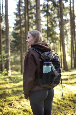 Translation missing: pl.Hiker in a forest carrying a backpack with a mint green Yeti bottle in the side pocket
