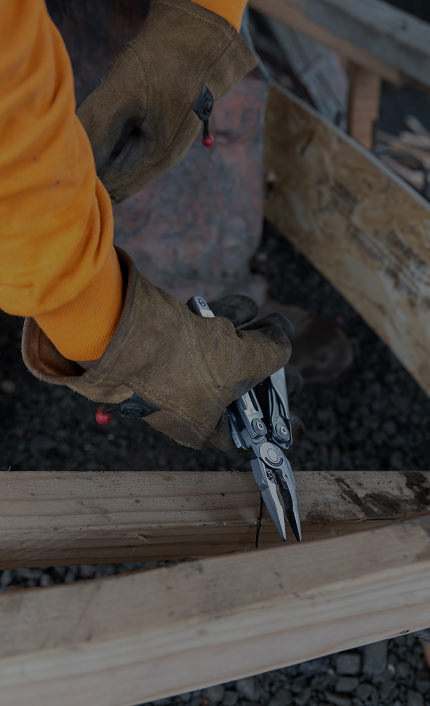 Translation missing: de.Tradesman in thick work gloves using the Leatherman Surge heavy-duty pliers to remove a nail from a 2x4