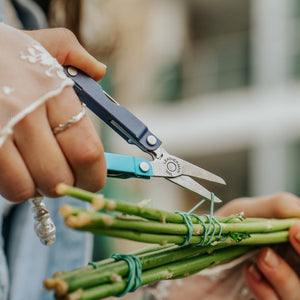 Translation missing: fr.Person using the scissors on a Leatherman Micra® in Lavender Mist color to cut the rubber band holding flower stems