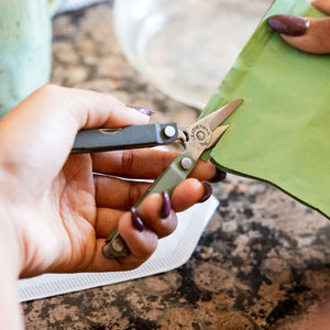 Translation missing: fr.A person using the scissors on a Spruce Leatherman Micra® to cut a green pouch