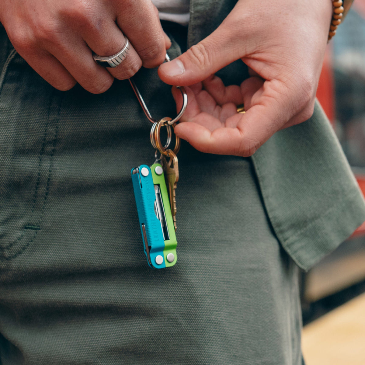 Translation missing: de.Person holding a keychain near a belt loop with a Leatherman Micra® in Teal Twist color on it, showcasing its compact design