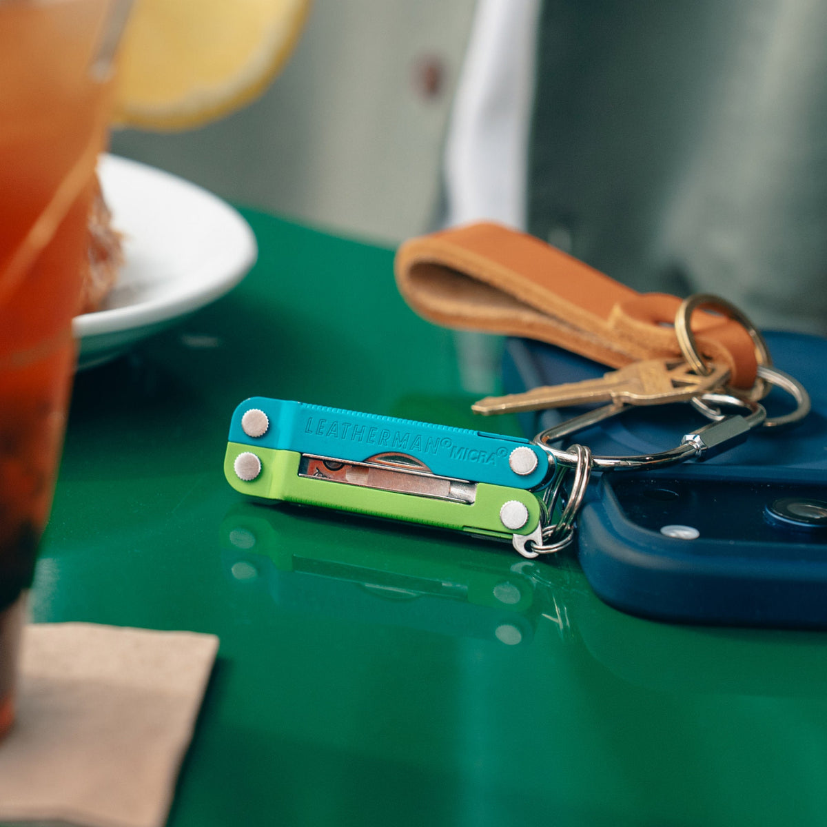 Translation missing: de.Leatherman Micra® in Teal Twist color attached to a keychain resting near a phone, showcasing its compact size