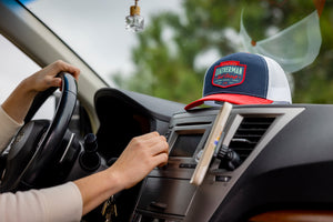 Translation missing: en.A person in a car with a navy Leatherman PNW Trucker Hat with a white mesh back and red brim resting on the dashboard