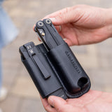 Translation missing: fr.Hands holding a black leather sheath carrying two black multitools outdoors