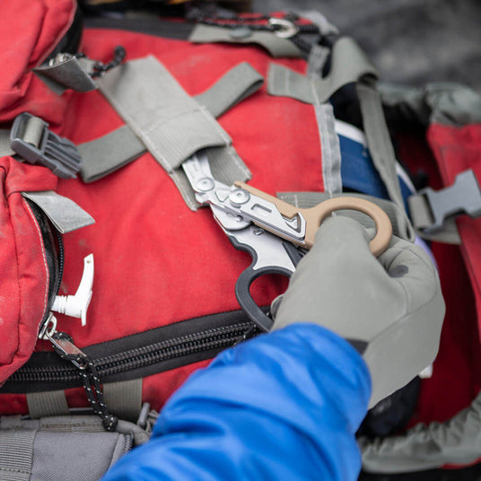 Translation missing: en.Person removing a Coyote/Black Leatherman Raptor® Rescue tool from a red backpack during an outdoor activity