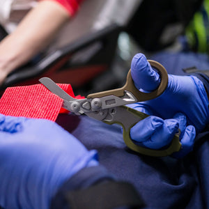 Translation missing: nl.Person using the shears on a Woodland Leatherman Raptor® Rescue to cut a piece of red gauze