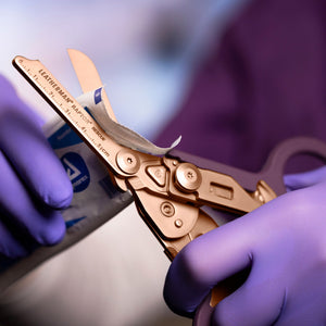 Translation missing: fr.Rose Gold Raptor® Rescue shears cutting open medical packaging held by gloved hands