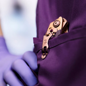 Translation missing: fr.Rose Gold Raptor® Rescue tool clipped to a purple scrub pocket held by a gloved hand