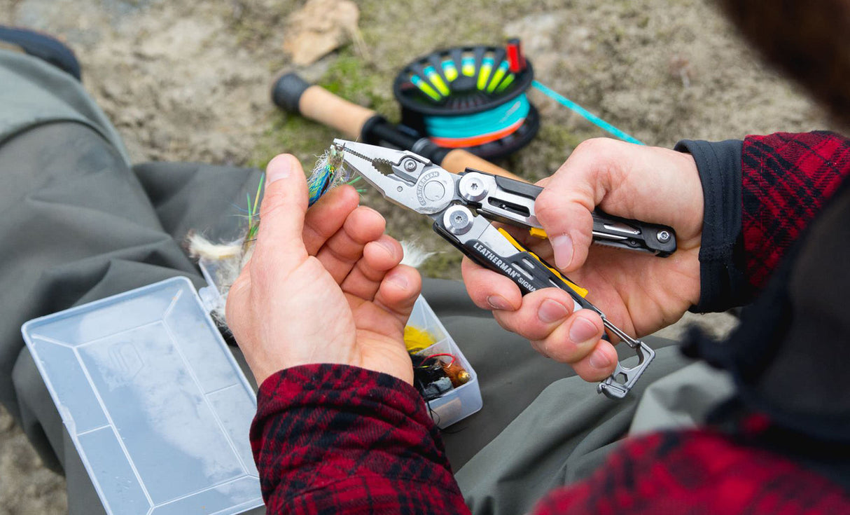 Translation missing: en.A person using the pliers on a black and stainless Leatherman Signal® multitool to grasp a fish hook