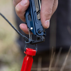 Translation missing: de.A person using the carabiner on a Nocturnal Leatherman Signal® to attach to a rope on a tent stake