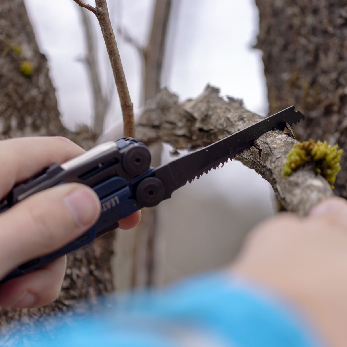 Translation missing: de.A person using the saw on a Nocturnal Leatherman Signal® to cut a branch