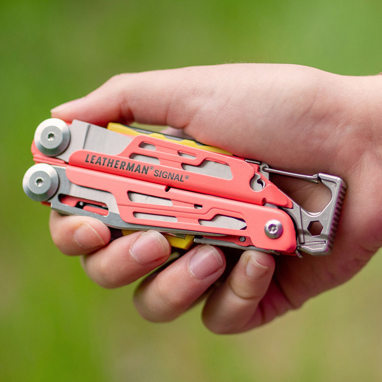 Translation missing: es.Hand holding a folded Guava Leatherman Signal multi-tool outdoors