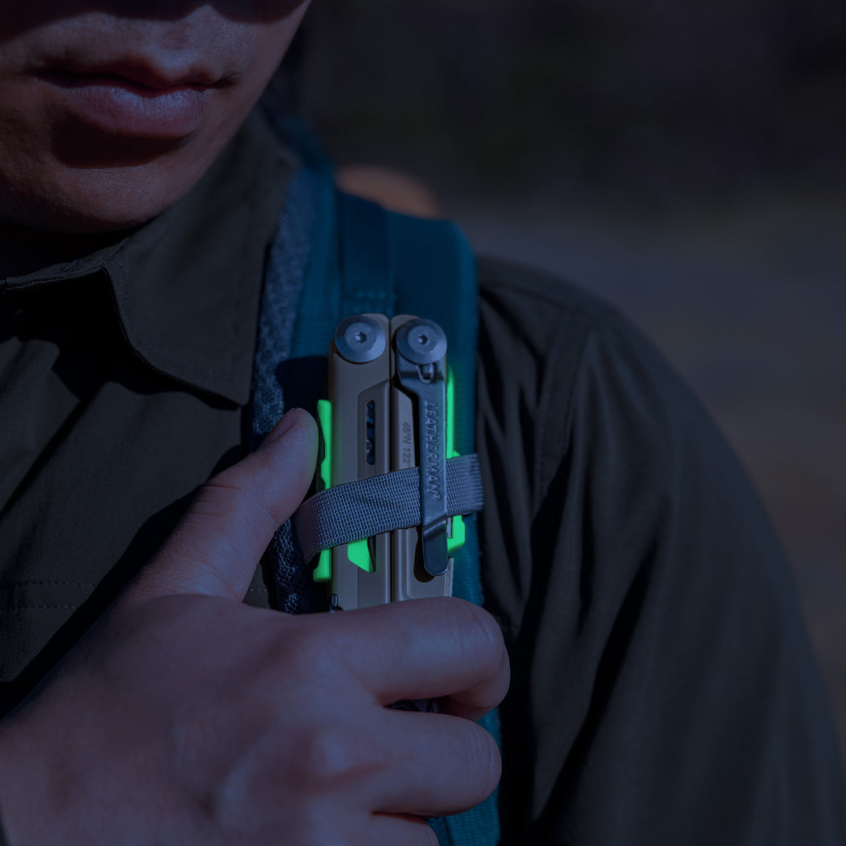 Translation missing: es.Person securing a Sandstorm multitool with neon accents to a backpack strap outdoors