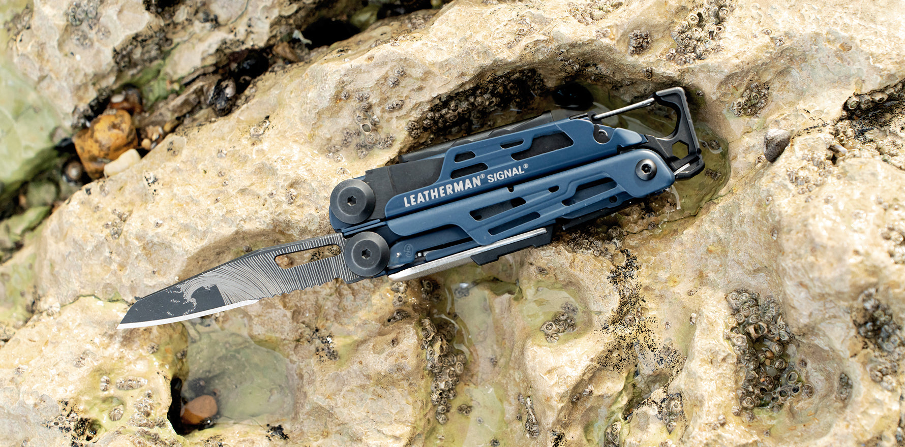 Leatherman Signal® World Artist Day 2026 multi‑tool shown open on natural rock, featuring blade and carabiner.