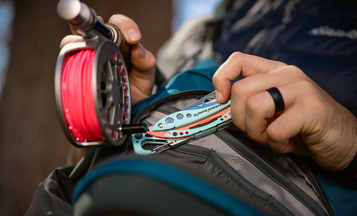 Translation missing: es.Person holding a Paradise Leatherman Skeletool® CX multi-tool next to a fishing pole and backpack