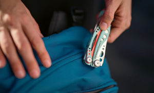 Translation missing: es.Hand holding a Paradise Leatherman Skeletool® CX multi-tool on top of a blue bag