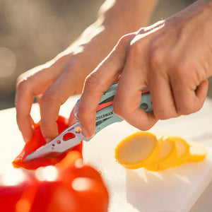 Translation missing: pl.Hands using a Paradise Leatherman Skeletool CX knife to slice red and yellow vegetables on a cutting board