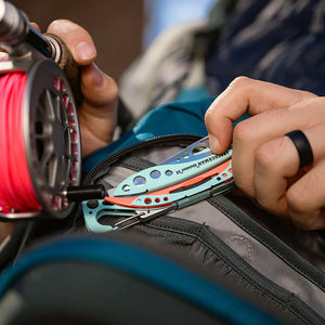 Translation missing: pl.Person holding a Paradise Leatherman Skeletool CX multitool next to a backpack while holding a fishing reel
