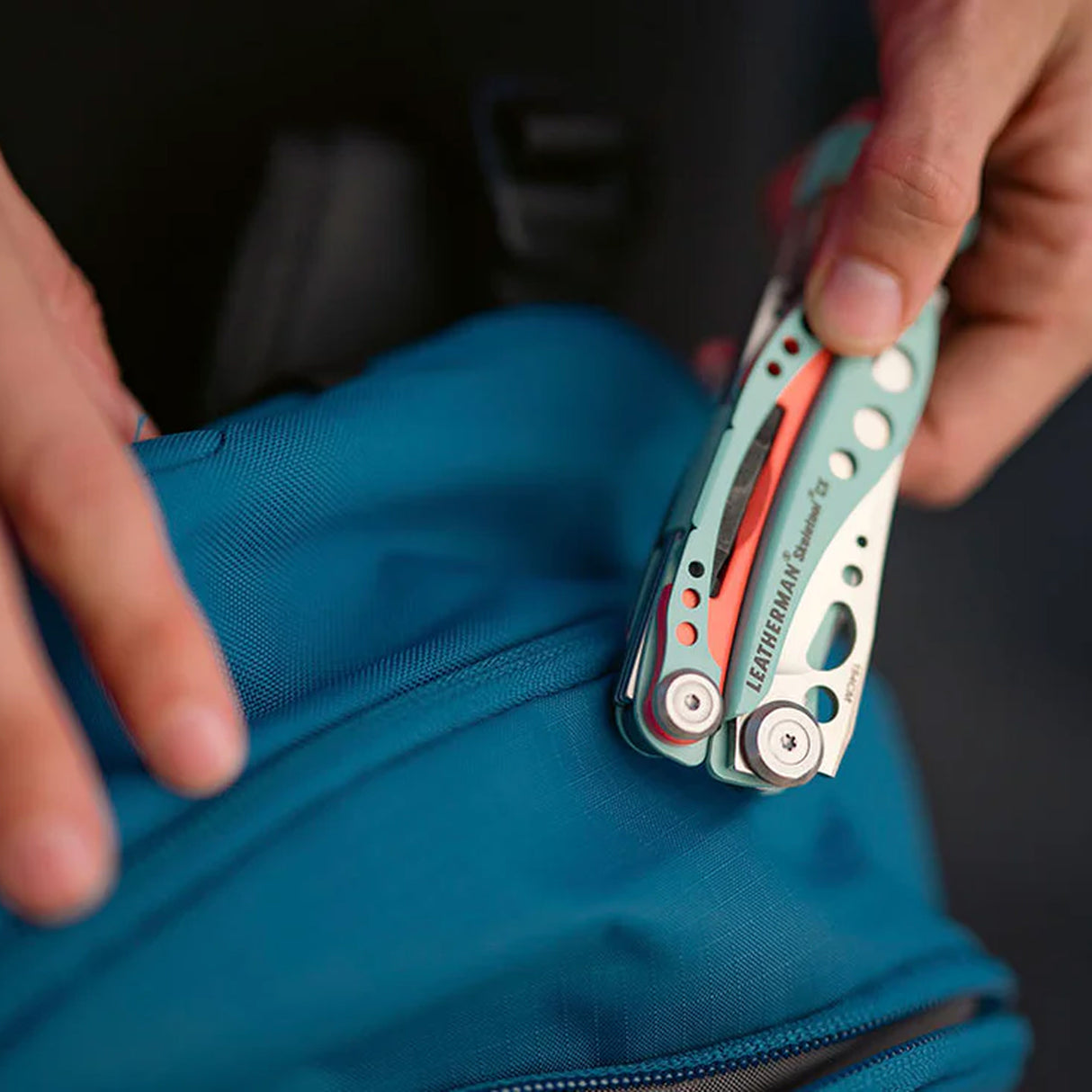Translation missing: pl.Hand holding a Paradise Leatherman Skeletool CX multitool over a blue backpack