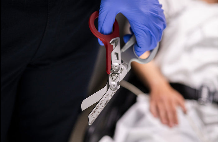 Translation missing: en.Garnet Leatherman Raptor Rescue multitool held in a gloved hand in front of a blurred medical background
