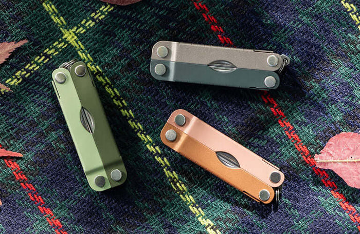 Translation missing: es.Three Micra® multitools in Cardamon, Ginger Peach, and North Star colors displayed on a plaid background with autumn leaves