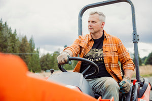 Translation missing: fr.A person wearing a black Leatherman Timber Tee driving a tractor outdoors