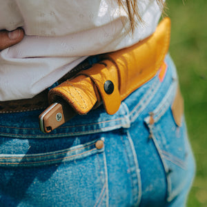 Translation missing: es.Earth Brown Leatherman Trac Knife handle sticking out of a Brown Leatherman Trac Knife Sheath with black snap closures that is attached to the back of a woman's belt