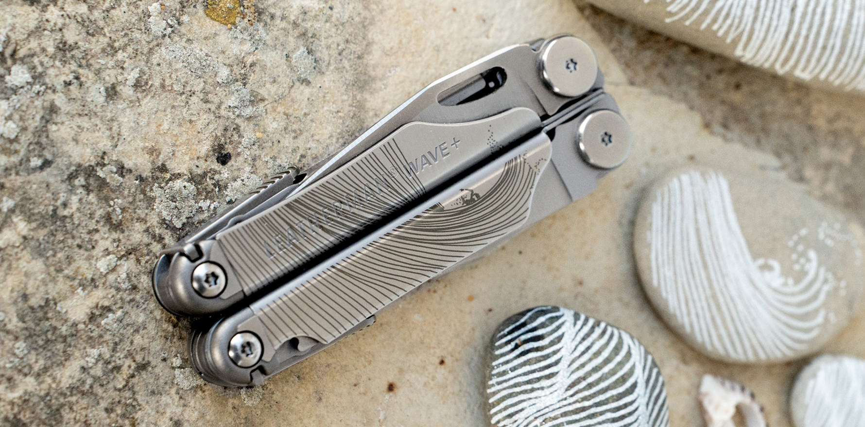 Stainless steel Leatherman Wave with a design by artist The Minimalist Wave next to stones with a similar design